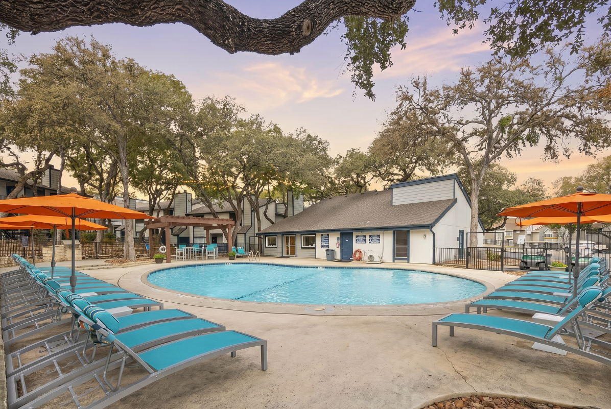 Swimming pool with lounge chairs and umbrellas at sunset at Elevate at Huebner Grove apartments